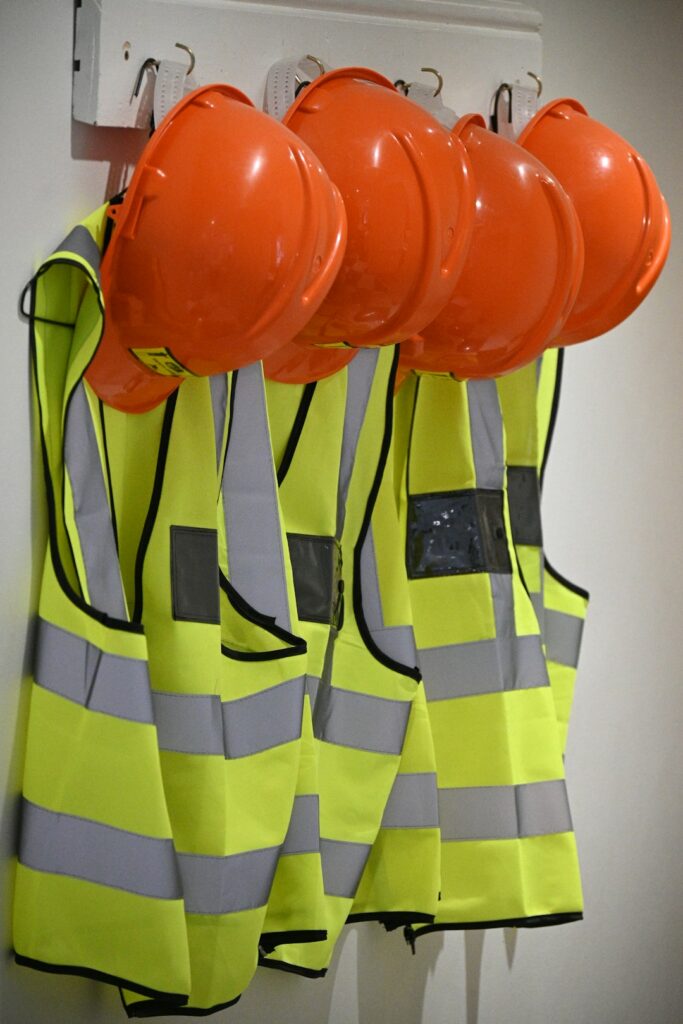 Four orange hard hats and neon yellow safety vests hanging on a wall
